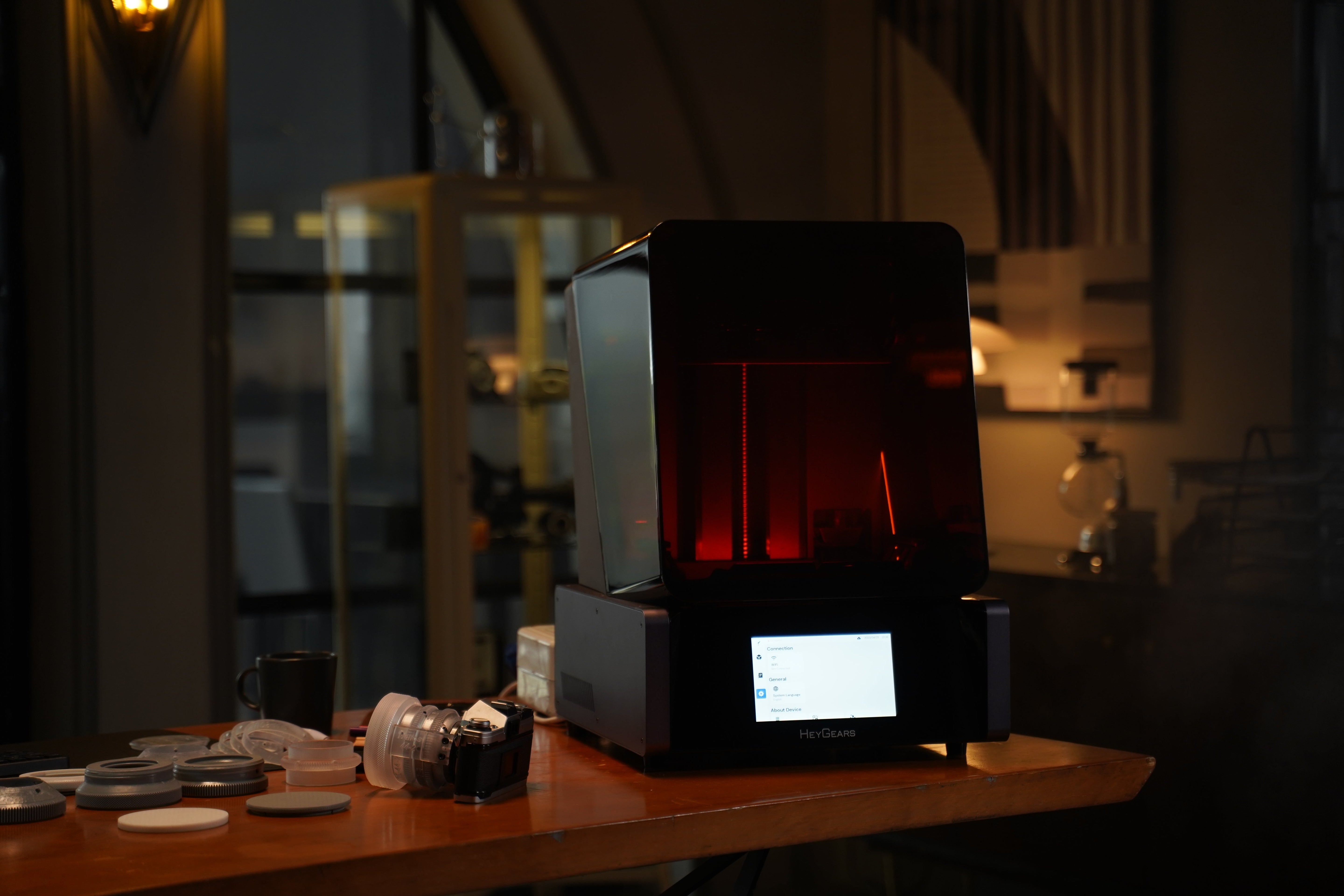 Desktop resin 3D printer glowing red on a workbench in a dimly lit studio.