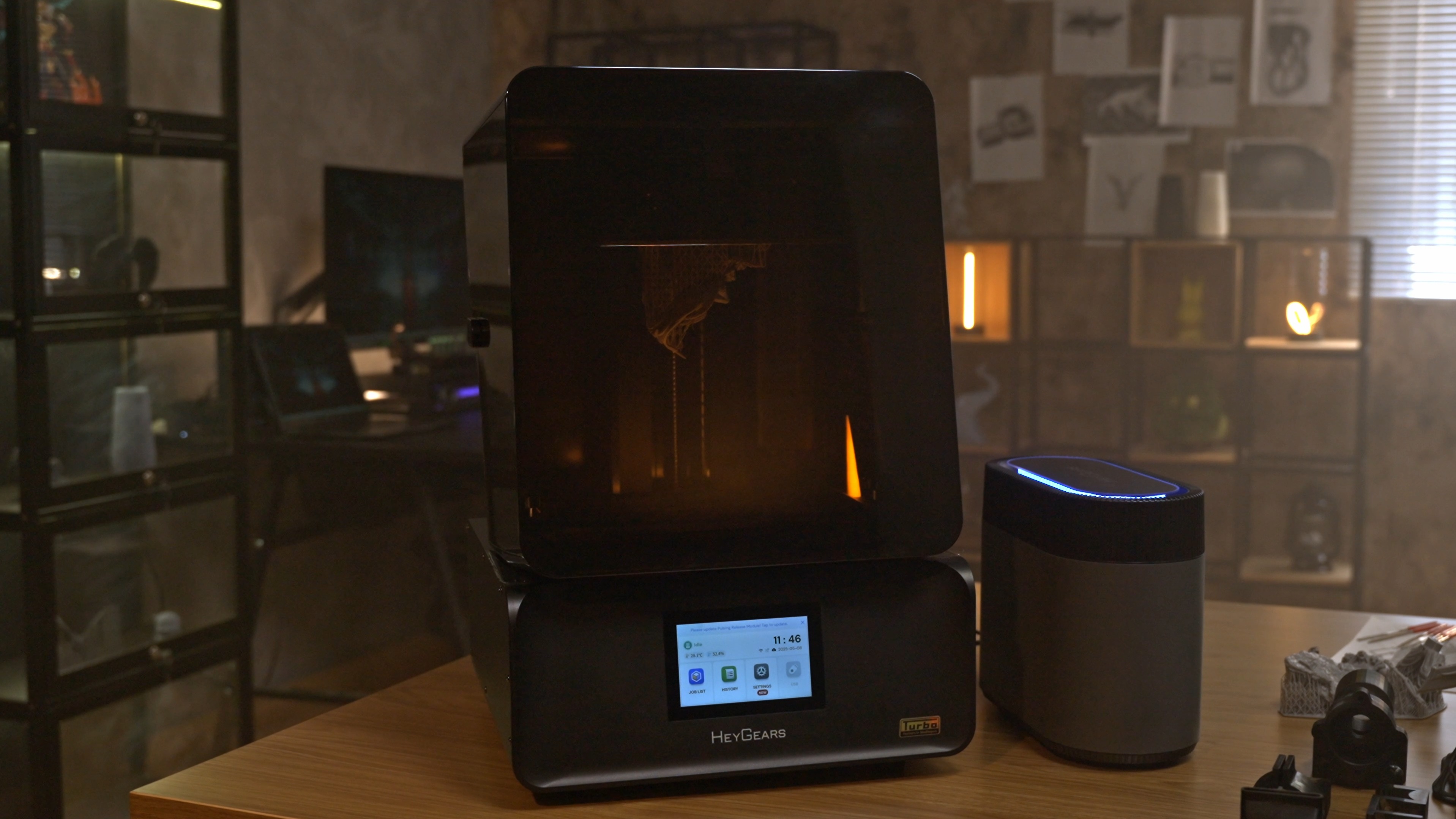 Desktop resin 3D printer with an amber cover and touchscreen, shown on a studio workbench.