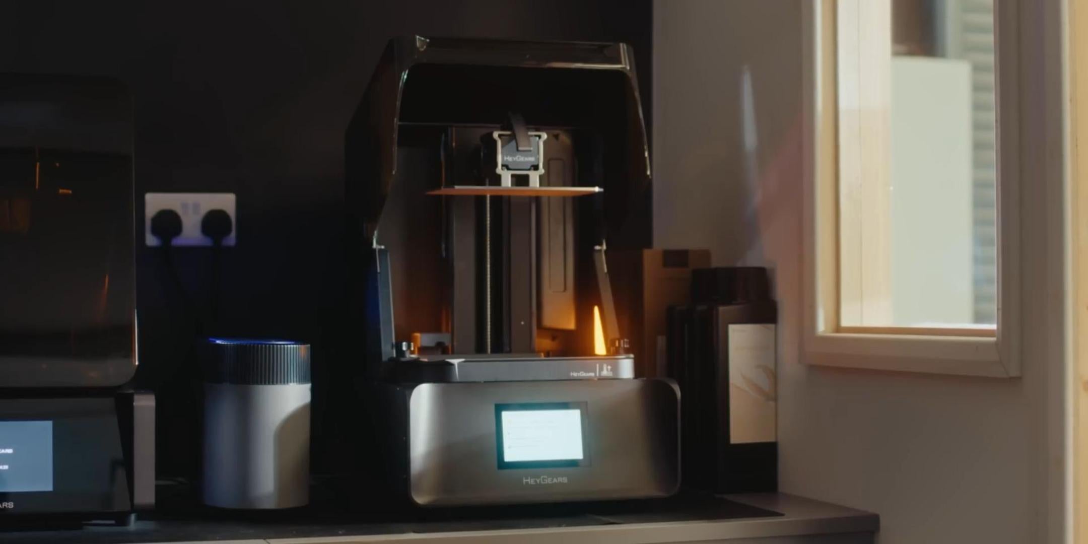 Desktop resin 3D printer beside resin bottles on a workbench, illustrating a string-free alternative to FDM printing.