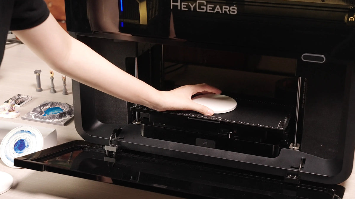 User placing a white circular item on the HeyGears G1X UV Edition flatbed to prepare for UV printing.