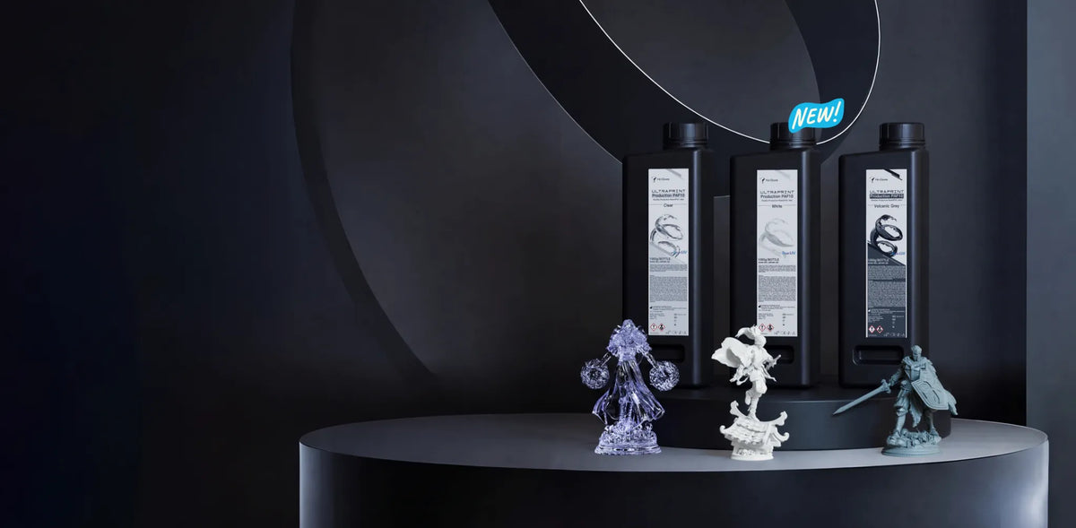 HeyGears PAF10 flexible resin in Clear, White, and Volcanic Gray displayed with detailed 3D printed miniature models.