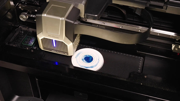 HeyGears G1X UV Edition printhead applying a blue circular design directly onto a white object using desktop UV printing.